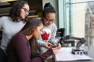 Three female students operating robotic equipment.