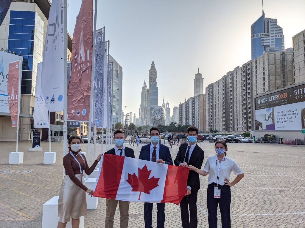 Erin Richardson and 4 members of her team holding a Canadian flag in Dubai with the skyline in the background
