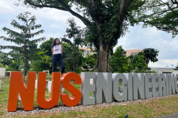Jasmine Chahal standing behind a large block text display that reads "NUS ENGINEERING".