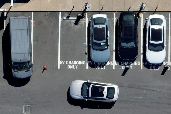 Seen from above, a Polestar electric car prepares to park at an EV charging station. Four other vehicles are parked in the charging station spots.