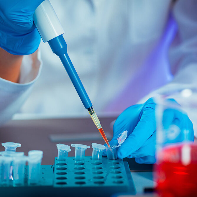 Scientist in PPE pipetting red solution into test tubes